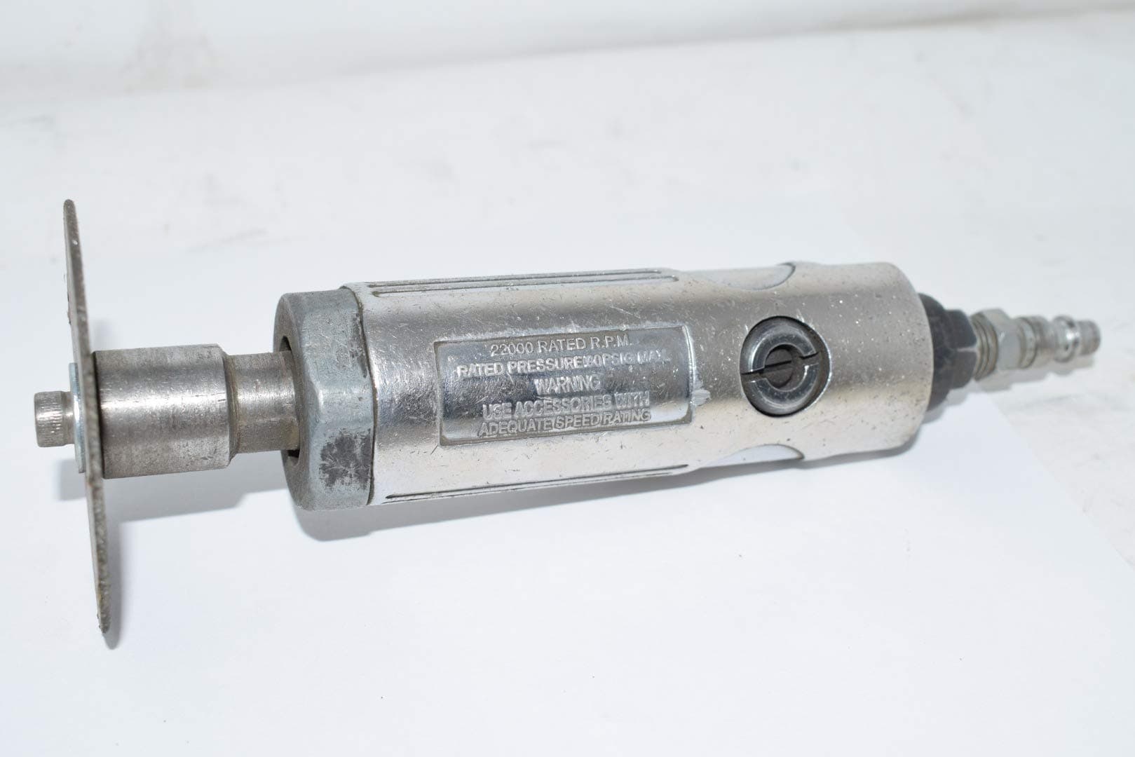 Metal pneumatic cutoff tool with a circular cutting disc on a white surface showing a label with RPM and pressure specifications.